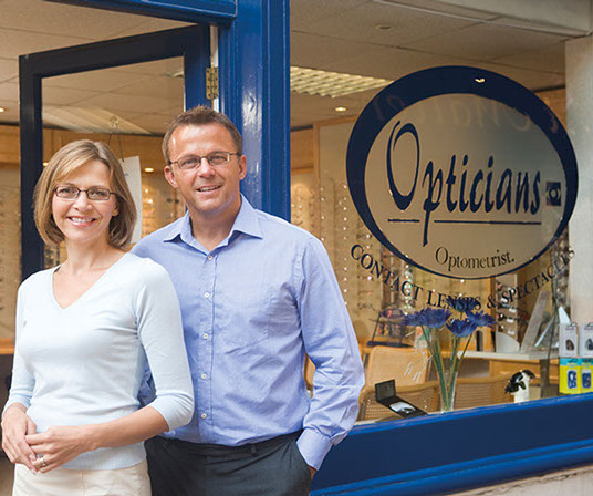 A photo of a male and a female optician stood in their practice doorway.
